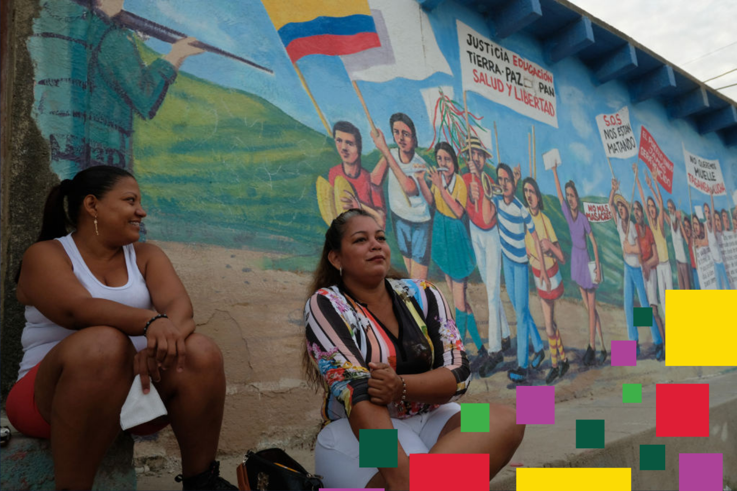 Local women sit and chat outside their home in front of a mural; a banner calls for justice, education, peace, bread, health and freedom; another reads "S.O.S They are killing us". August 11, 2021 in Taganga, Colombia.