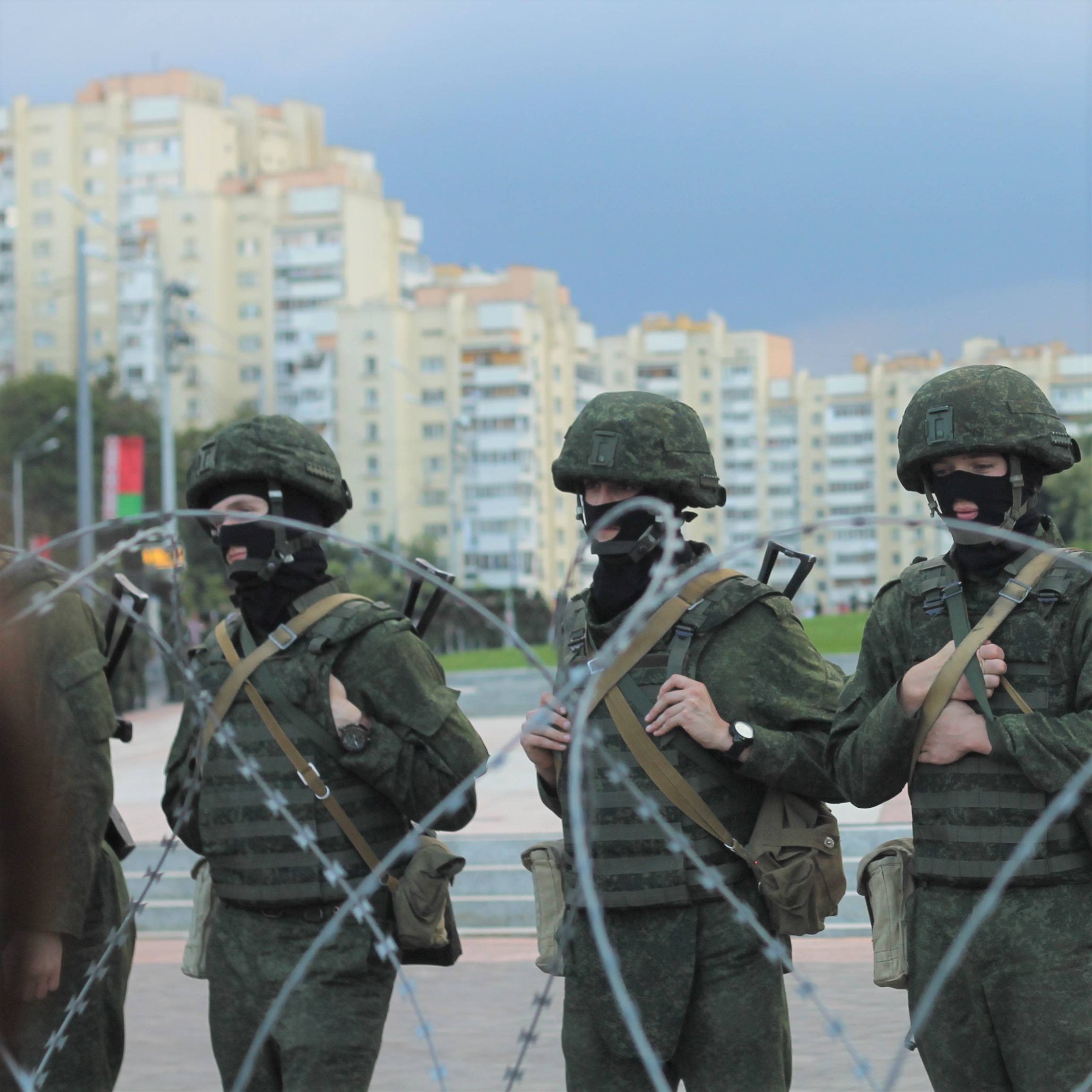 Armed individuals in military-style uniforms stand behind a fence of barbed wire at a protest rally in Minsk, Belarus in August 2020. Photo by Natallia Rak via Flickr