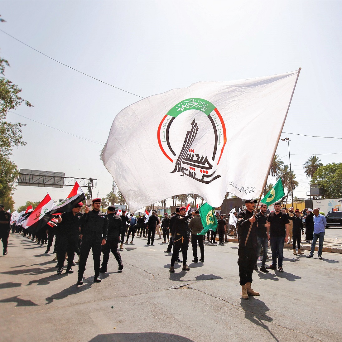 Members of Iraq's Popular Mobilization Forces hold flags during a symbolic funeral of members of PMF, who were killed by US air strikes on the Syria-Iraq border (Baghdad, June 2021). Photo: REUTERS/Saba Kareem