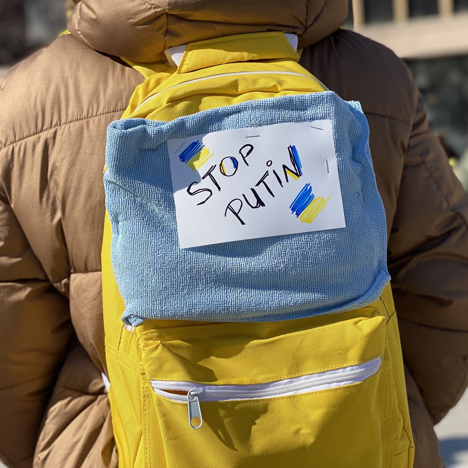 A yellow backpack with a handmade sign attached that reads "Stop Putin" is worn by a protester at the Wisconsin State Capitol in Madison (United States), 2022. Image: Chali Pittman / WORT News 12
