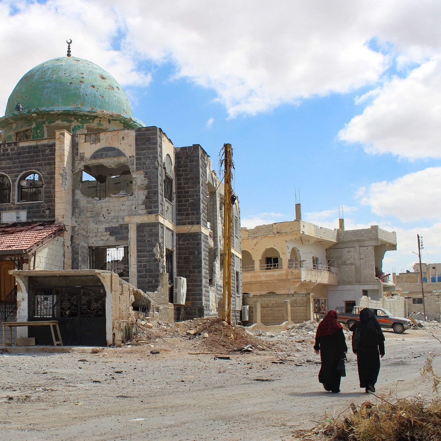 Women walk past a mosque, damaged during clashes between rebels and regime forces, in Syria's southern city of Daraa on 11 September 2021.