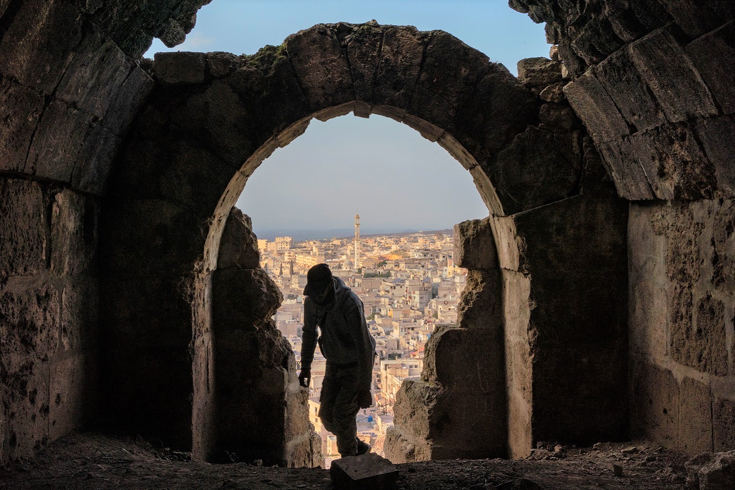 A Syrian visits the castle of Harim, which has been damaged by a recent earthquake, with a view of the city of Idlib in the background (February 2023)