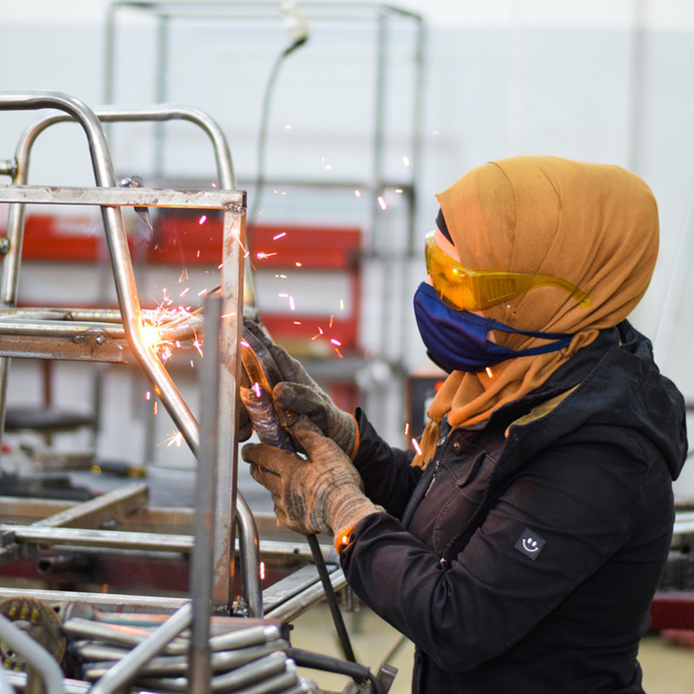 Aya welding an assistive chair at the Hand in Hand Charity workshop