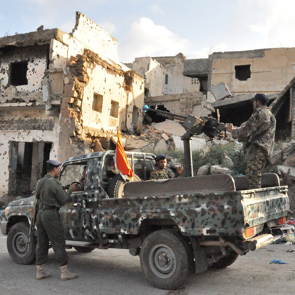 Soldiers in Taiz, Yemen, operate a gun on an armoured vehicle in front of a destroyed building.