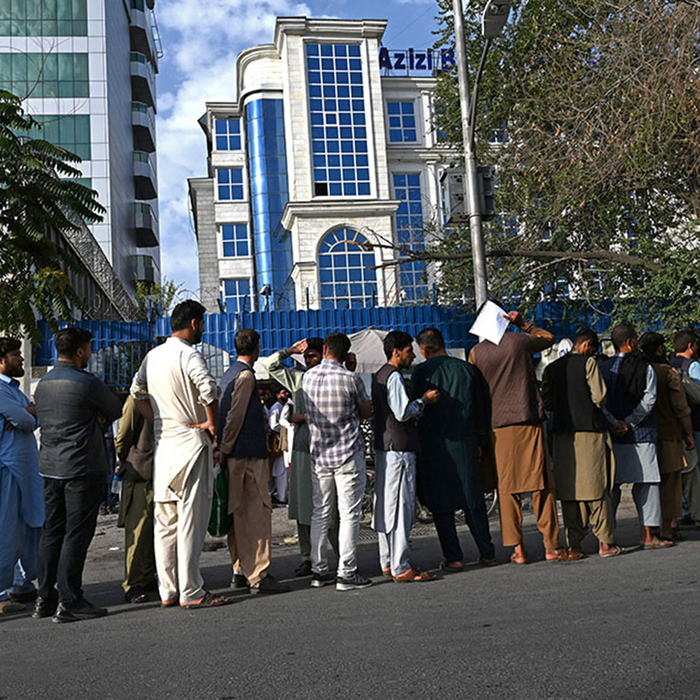 Afghan people stand in a queue as they wait for their turn to collect money from an ATM