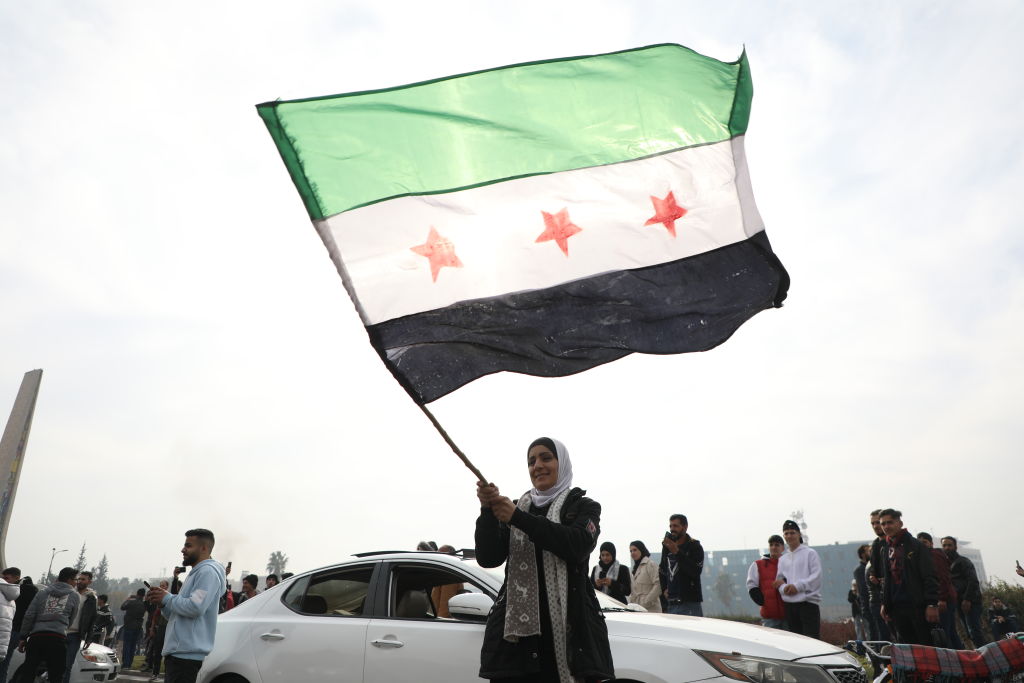 A woman waves the flag of the Syrian rebels as people gather to celebrate the fall of the government in Damascus